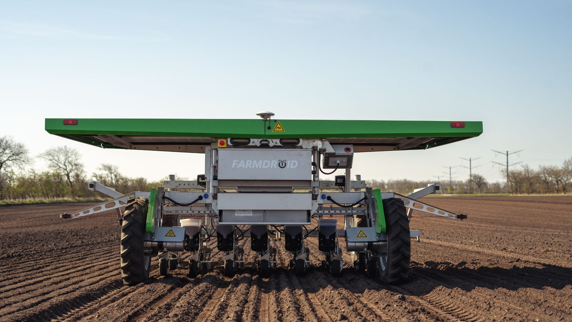 Farmdroid autonomous planting robot operating in a freshly tilled field, with green solar panel roof and multiple seeding units.