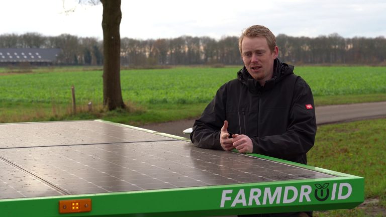 Gert Sterenborg standing by his FarmDroid robot by a chicory field, talking about his experience with precision weeding and targeted spraying to reduce chemical use.